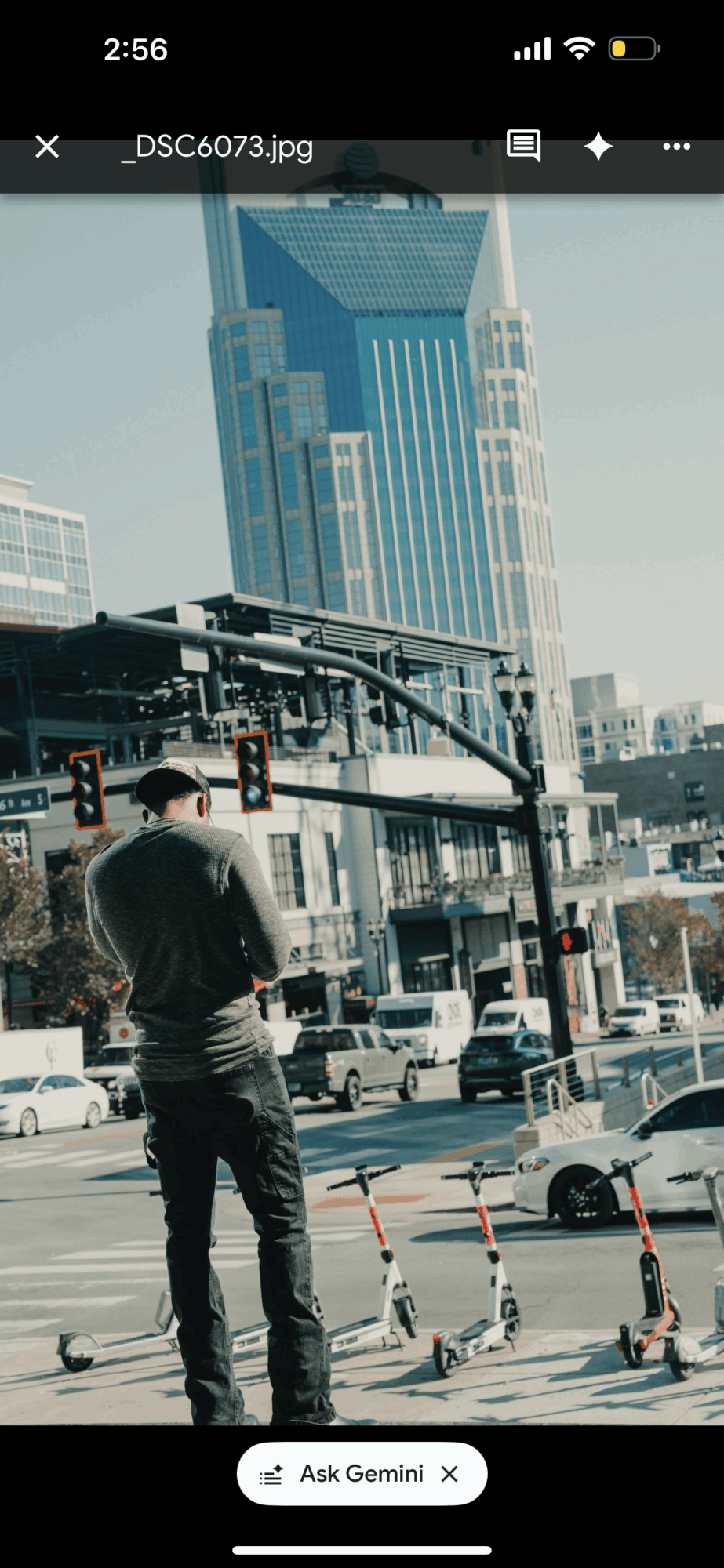Person standing on city street with tall buildings and traffic lights in background.
